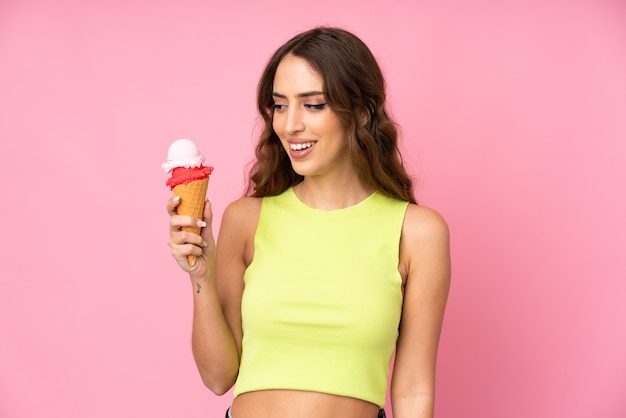 Joven mujer sosteniendo un helado de cucurucho en un rosa con expresión feliz