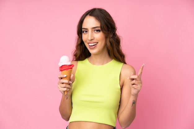 Joven mujer sosteniendo un helado de cucurucho sobre una pared rosa apuntando hacia una gran idea