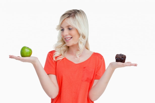 Joven mujer sosteniendo una manzana y un panecillo mientras mira a la manzana