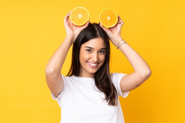 Joven mujer sosteniendo una naranja sobre pared amarilla aislada