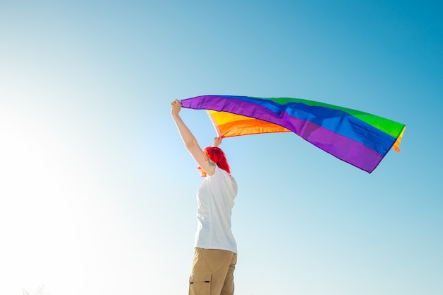 Joven mujer sosteniendo ondeando la bandera LGBT sobre la cabeza