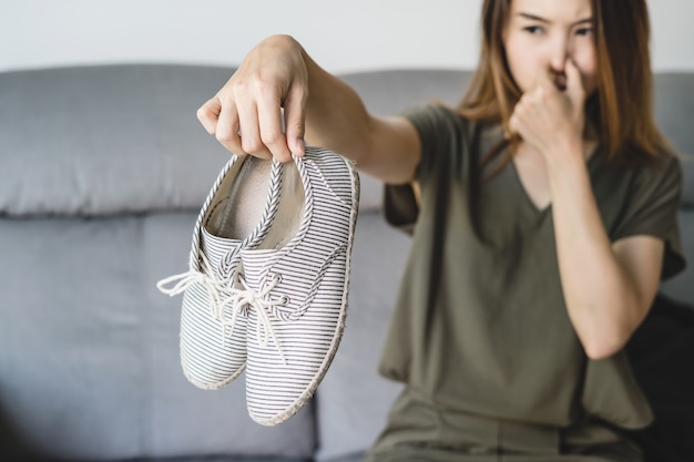 Foto joven mujer sosteniendo un par de zapatos malolientes