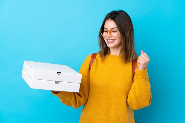 Joven mujer sosteniendo una pizza cajas sobre pared azul aislado