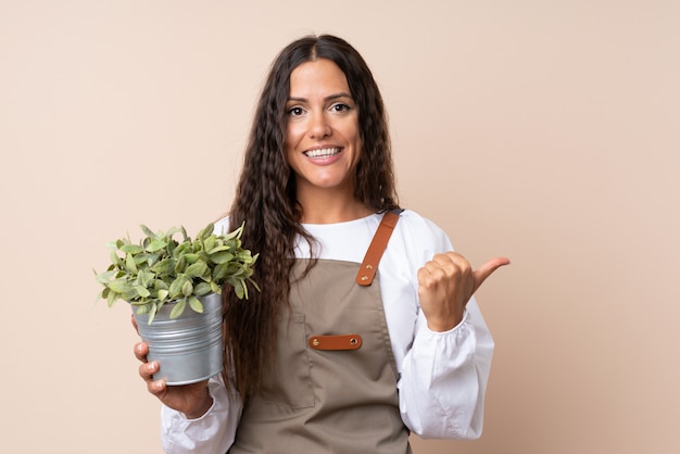 Joven mujer sosteniendo una planta apuntando hacia un lado para presentar un producto