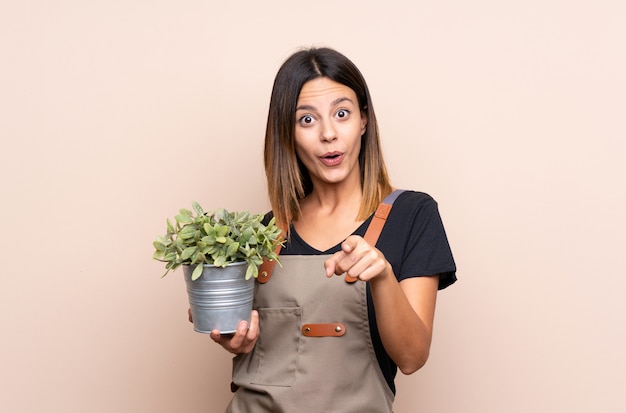 Joven mujer sosteniendo una planta sorprendida y apuntando al frente