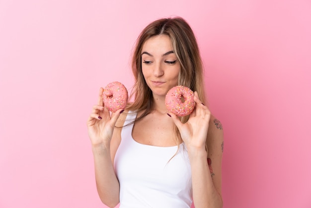 Joven mujer sosteniendo una rosquilla sobre pared aislada