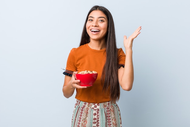 Joven mujer sosteniendo un tazón de cereal celebrando una victoria o éxito