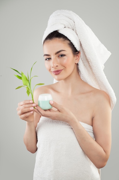 Joven Mujer Spa después de Sauna Modelo de Spa Sonriente con Crema Hidratante Piel Clara Toalla Blanca y Hojas de Bambú Verde Concepto de Cuidado de la Piel