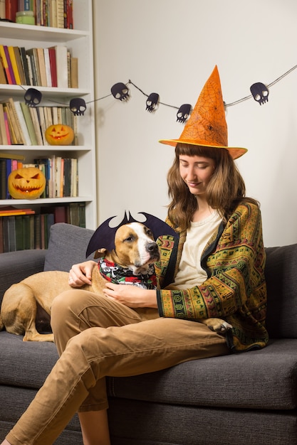 Joven mujer con su mascota en el sofá en la sala vestida para la fiesta de halloween