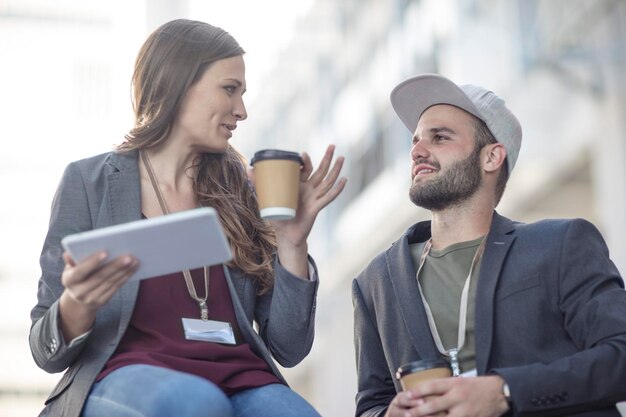 Joven y mujer con tableta y café para ir a hablar al aire libre