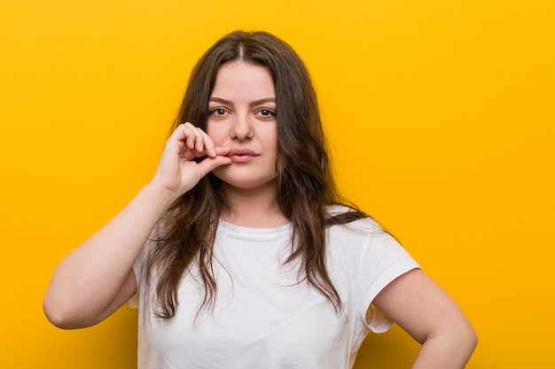 Joven mujer de talla grande con curvas con los dedos en los labios guardando un secreto.