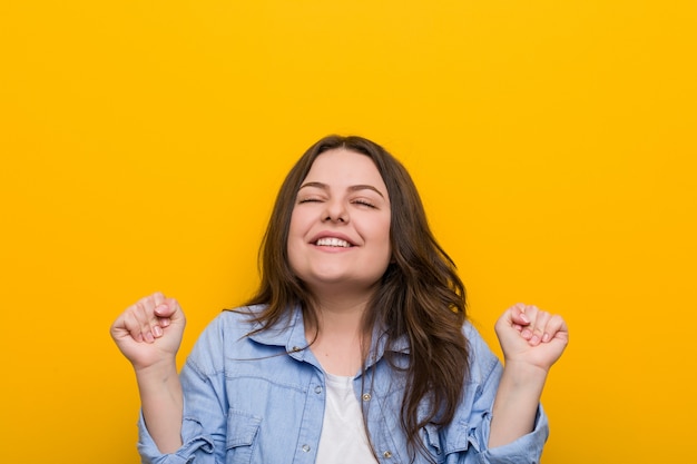 Foto joven mujer de talla grande con curvas levantando el puño, sintiéndose feliz y exitoso.