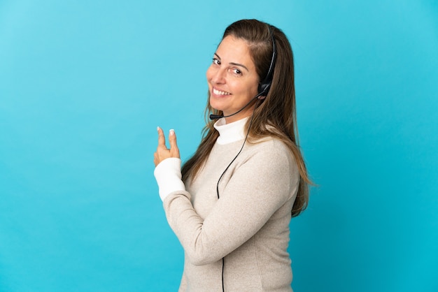 Foto joven mujer de telemarketing sobre pared azul aislada apuntando hacia atrás
