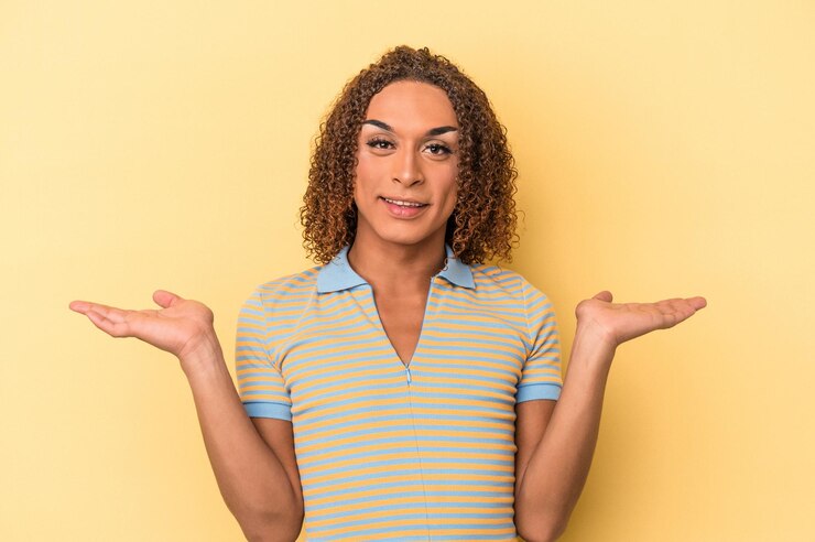 Foto joven mujer transexual latina aislada de fondo amarillo hace escala con los brazos, se siente feliz y confiada.
