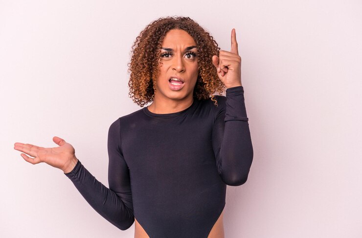 Foto joven mujer transexual latina aislada de fondo rosa sosteniendo y mostrando un producto a mano.