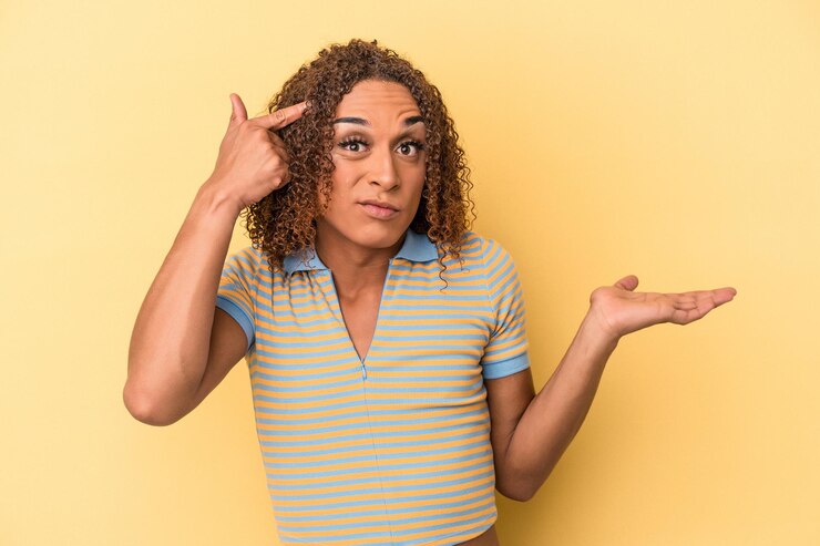 Foto joven mujer transexual latina aislada sobre fondo amarillo sosteniendo y mostrando un producto en la mano.