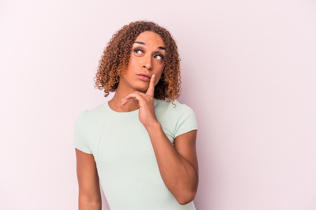 Joven mujer transexual latina aislada sobre fondo rosa contemplando, planificando una estrategia, pensando en la forma de un negocio.