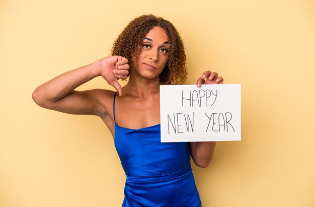 Joven mujer transexual latina celebrando el año nuevo aislado sobre fondo amarillo mostrando un gesto de aversión, pulgares hacia abajo. Concepto de desacuerdo.