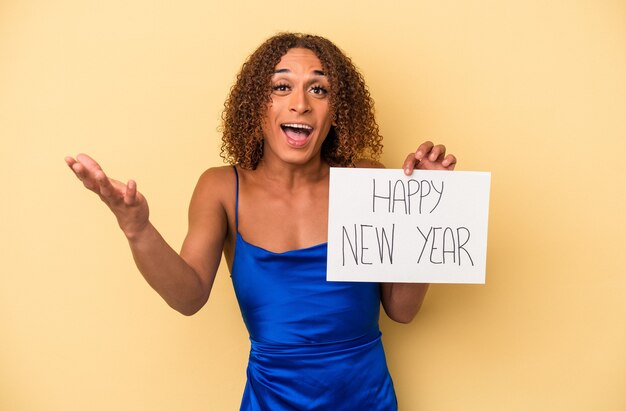 Joven mujer transexual latina celebrando el año nuevo aislado sobre fondo amarillo recibiendo una agradable sorpresa, emocionada y levantando las manos.