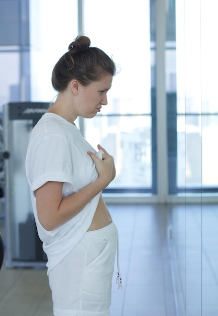 Joven mujer triste y disgustada está decepcionada por el vientre gordo mirando al espejo con frustración