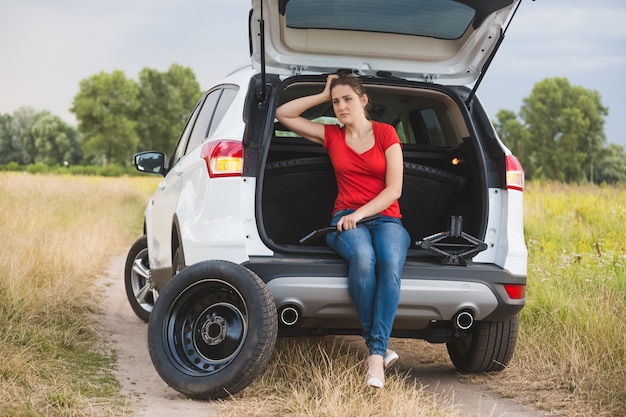 Joven mujer triste sentada en el coche roto en el campo