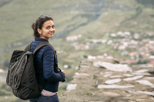 Joven mujer turista sonriente con una mochila con el telón de fondo de las montañas del Cáucaso, Georgia en un día brumoso