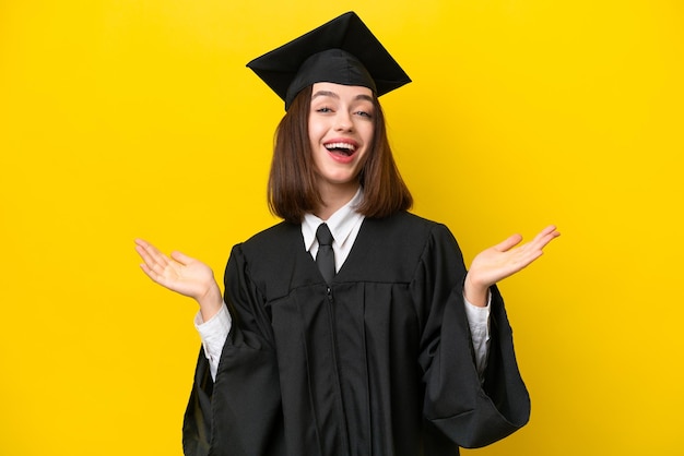 Joven mujer ucraniana graduada de la universidad aislada de fondo amarillo con expresión facial sorprendida