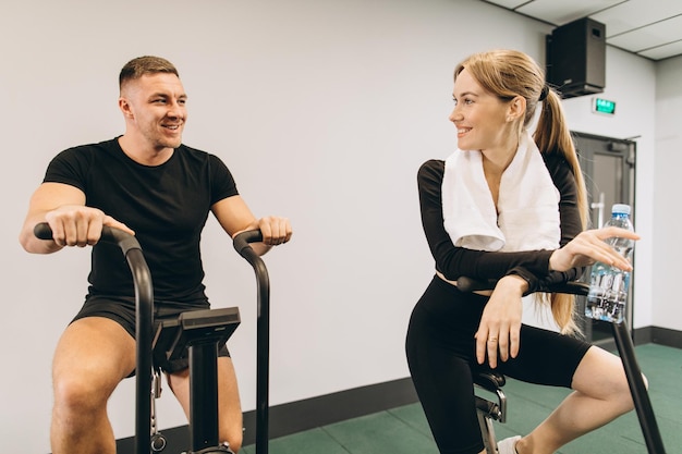 Joven y mujer usando bicicleta de aire para hacer ejercicio cardiovascular en el gimnasio de entrenamiento cruzado