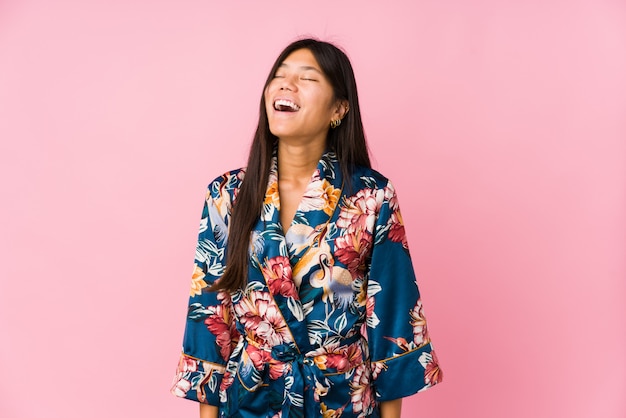 Joven mujer vestida con un kimono pijama relajado y feliz riendo, cuello estirado mostrando los dientes.