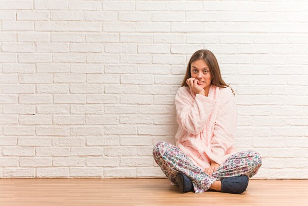 Joven mujer vestida con pijama mordiéndose las uñas, nerviosa y muy ansiosa