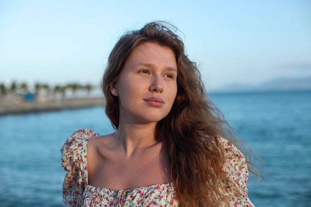 Joven mujer vestida con un vestido se encuentra en el paseo marítimo y disfruta de un cálido día de verano