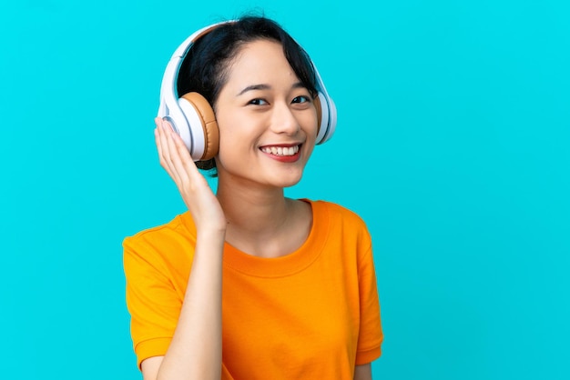 Joven mujer vietnamita aislada sobre fondo azul escuchando música