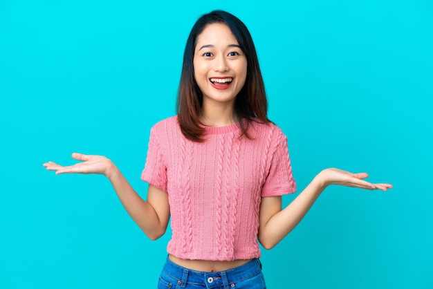 Joven mujer vietnamita aislada sobre fondo azul con expresión facial conmocionada