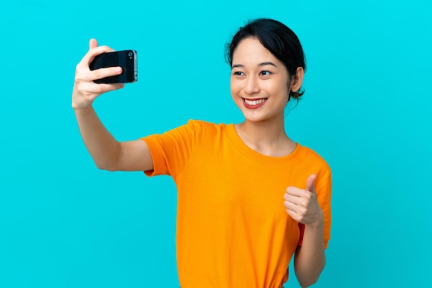 Joven mujer vietnamita aislada sobre fondo azul haciendo un selfie con teléfono móvil