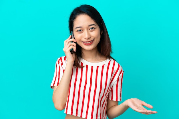 Joven mujer vietnamita aislada sobre fondo azul manteniendo una conversación con el teléfono móvil con alguien