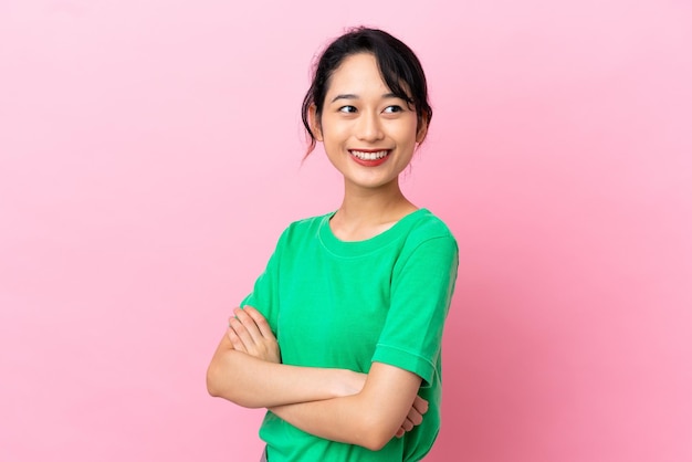 Joven mujer vietnamita aislada sobre fondo rosa con los brazos cruzados y mirando hacia adelante