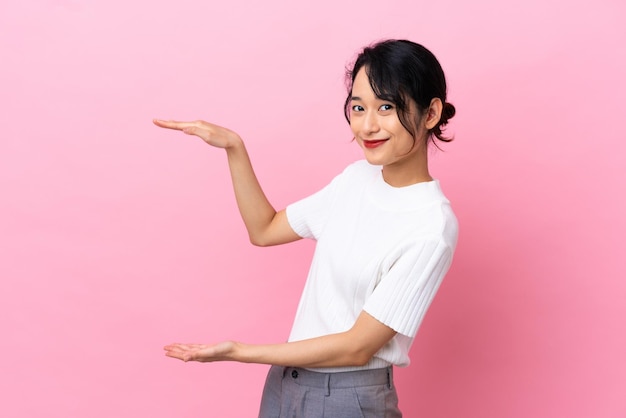 Joven mujer vietnamita aislada sobre fondo rosa sosteniendo copyspace para insertar un anuncio