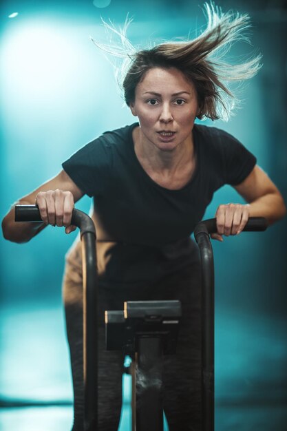 Foto una joven musculosa está haciendo un duro entrenamiento de crossfit en bicicleta en el gimnasio.