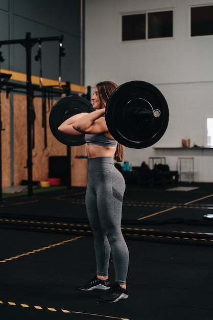 Joven musculosa levantando una barra de peso muerto en un gimnasio crossfit