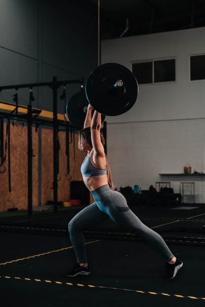 Joven musculosa levantando una barra de peso muerto en un gimnasio crossfit