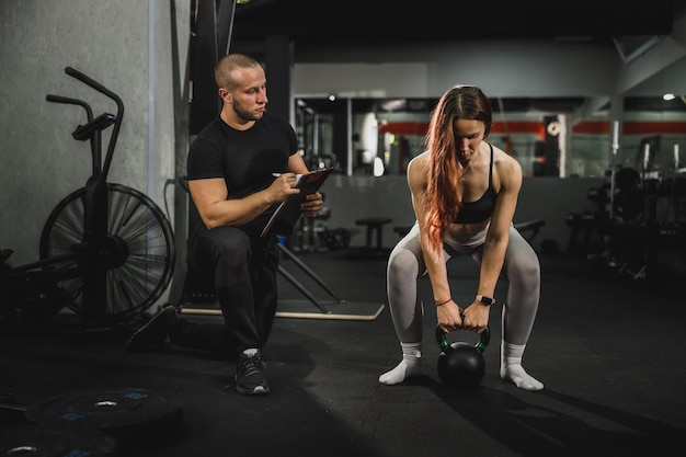 Joven musculosa trabajando con entrenador en el gimnasio. Ella está bombeando su músculo con pesas rusas.