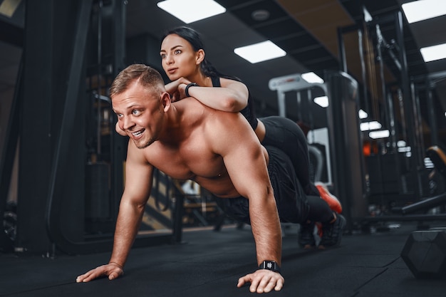 Joven musculoso haciendo ejercicio de flexión de brazos y sosteniendo a niña lecciones grupales de formación conjunta teambuilding romance