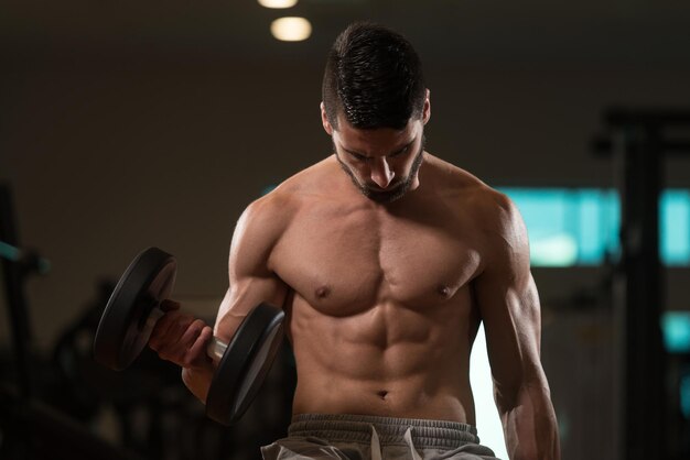 Joven musculoso haciendo ejercicio de peso pesado para bíceps con pesas en el gimnasio