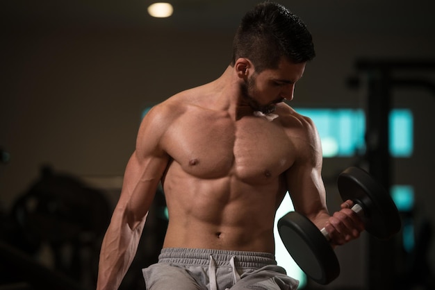 Joven musculoso haciendo ejercicio de peso pesado para bíceps con pesas en el gimnasio