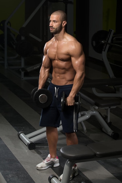 Joven musculoso haciendo ejercicio de peso pesado para los hombros en el gimnasio