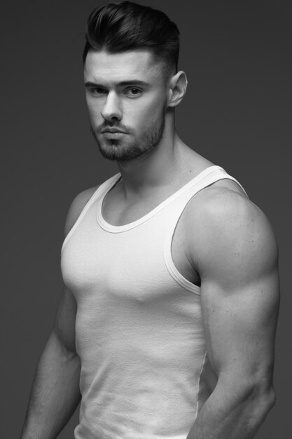 Foto joven musculoso hombre joven con barba. un hombre con camiseta. retrato masculino sobre un fondo gris. hombre elegante foto en blanco y negro hombre de deportes modelo de fitness masculino. retrato de estudio