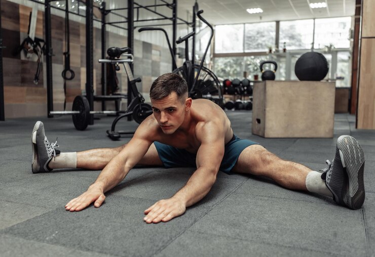 Joven musculoso practicando estiramientos musculares en un club de salud moderno