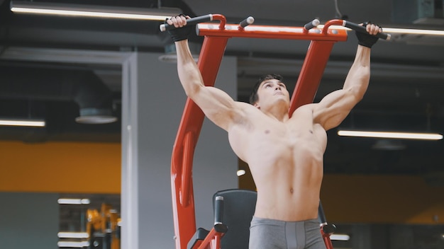 Foto joven musculoso tirando hacia arriba en un gimnasio, vista cercana