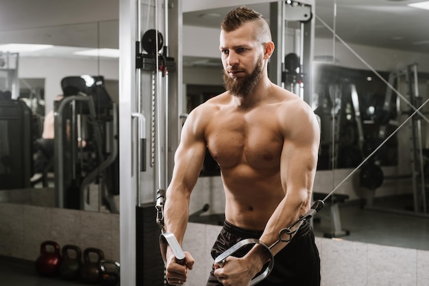 Joven musculoso trabajando en el gimnasio haciendo ejercicios de tríceps