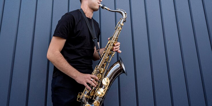Foto joven músico callejero tocando el saxofón cerca de la gran pared azul